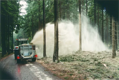 Stöckl trailer-mounted side spreader spreading lime in a forest