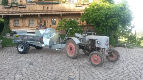 Stöckl trailer-mounted side spreader on a vintage tractor in front of an old farmhouse